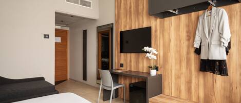 Una habitación de hotel moderna con cama, escritorio, silla, televisor y perchero.