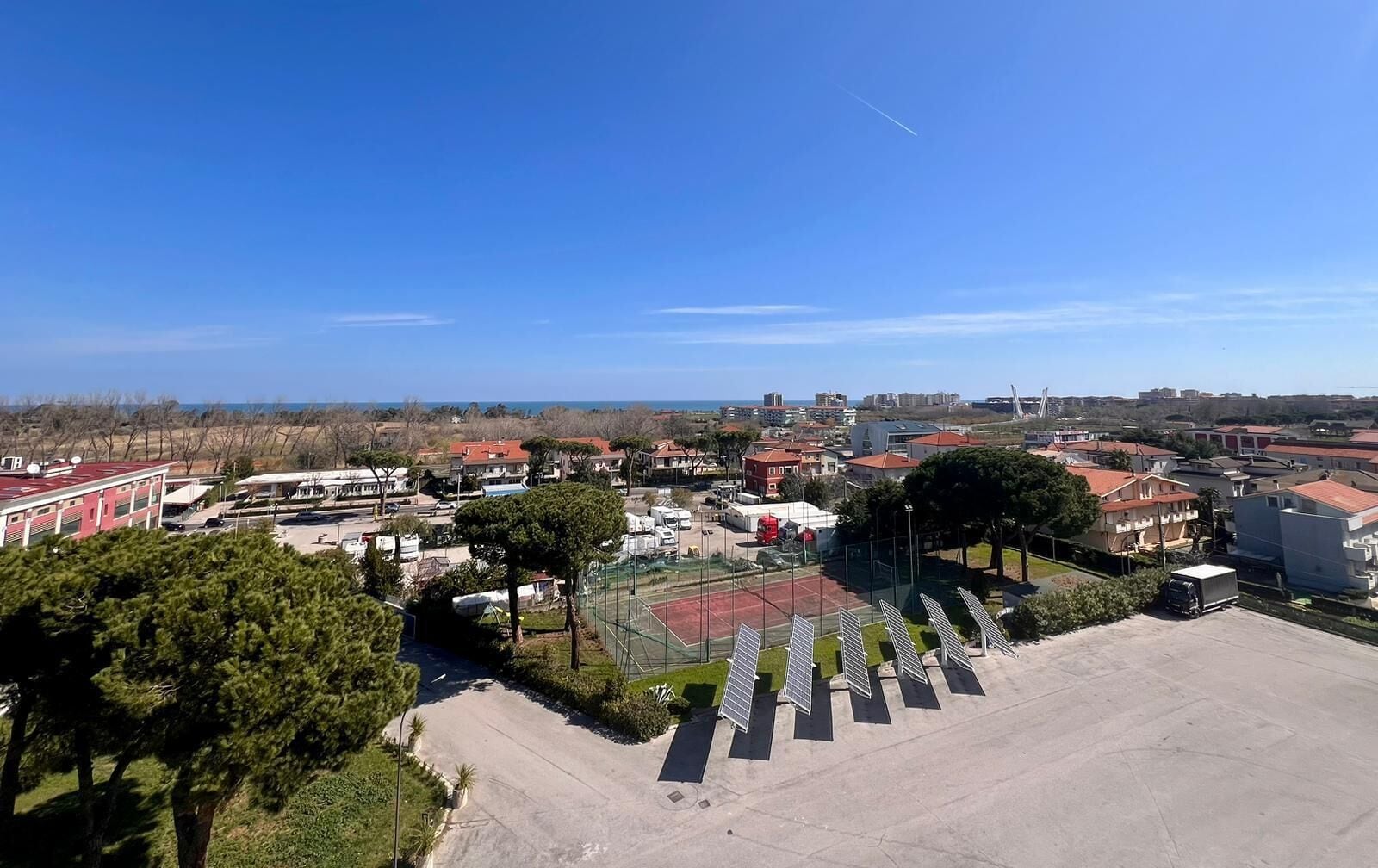 Vista aérea de uma área residencial com casas, quadra de tênis e painéis solares.