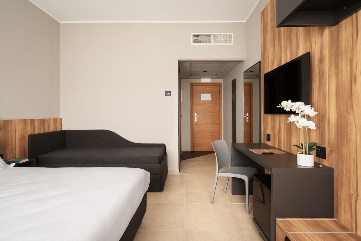 Una habitación de hotel moderna con cama, escritorio, silla, televisión y una planta en maceta.