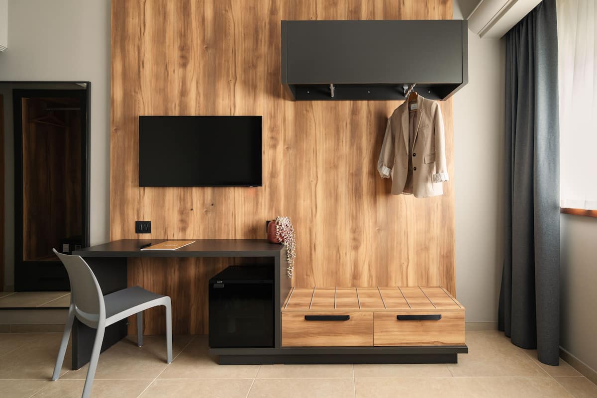 Una habitación moderna con pared de madera, un televisor de pantalla plana, un escritorio con silla y un perchero con una chaqueta.