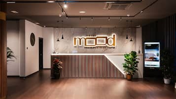 Ein Hotel-Empfangsbereich mit modernem Design, der eine Marmorwand, einen Empfangstresen und einen digitalen Bildschirm mit Hotelinformationen zeigt.