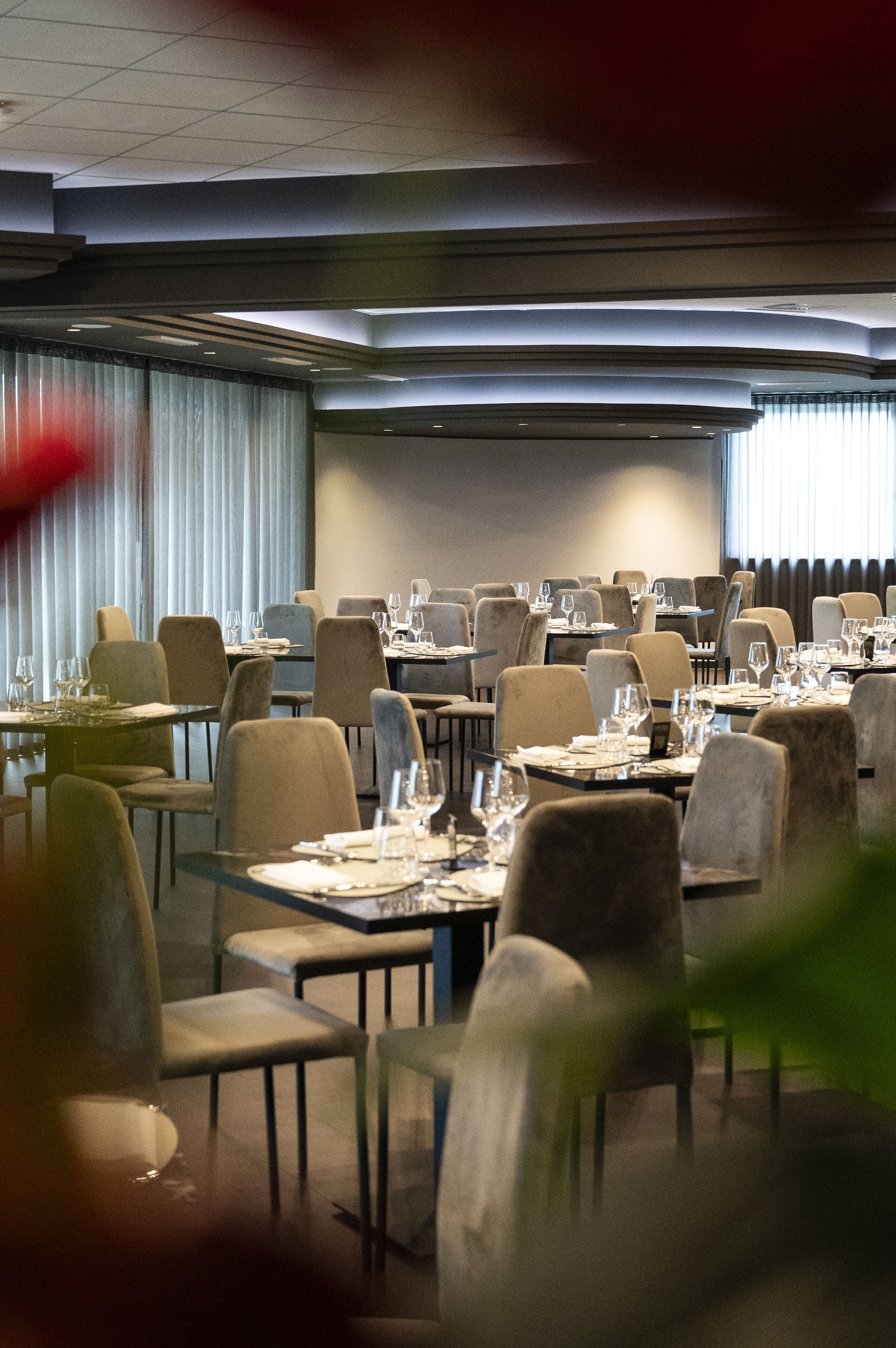 Un salón de conferencias con mesas dispuestas para una reunión, equipado con sillas y mesas, y una pantalla grande al frente.