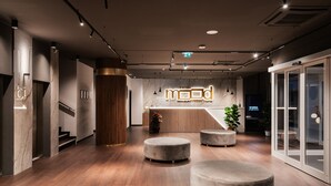 Un moderno vestíbulo de hotel con mostrador de recepción, suelo de madera y zonas de estar circulares.