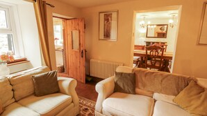 A cozy living room with two sofas, a radiator, and a dining area with wooden furniture. - White House (Penrith)