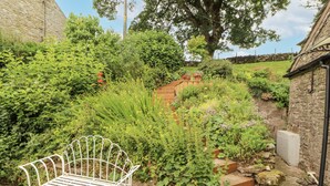 A garden with a stone wall, a metal bench, and various plants. - White House (Penrith)