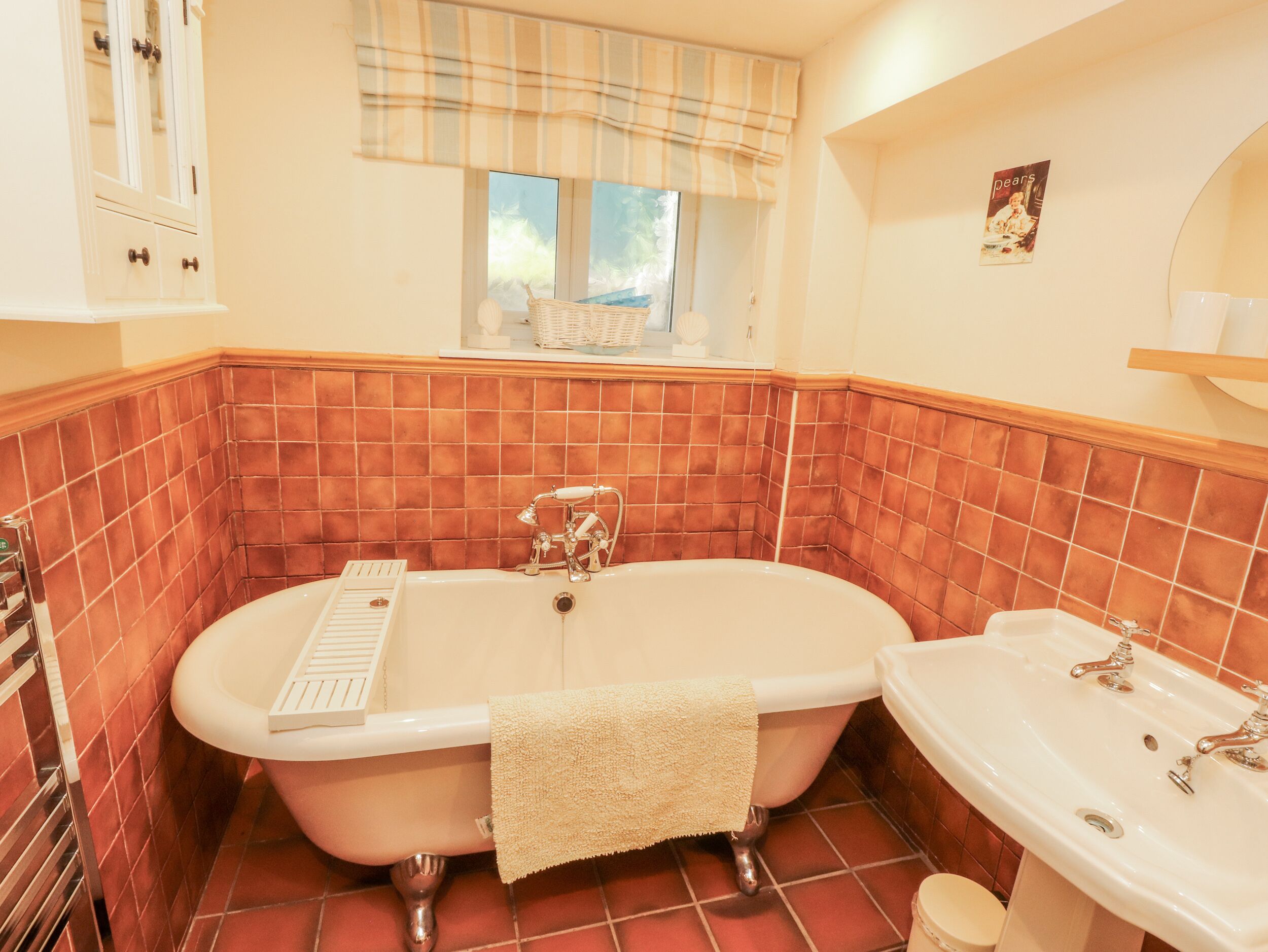 Une salle de bain avec une baignoire sur pieds, un lavabo et une fenêtre donnant sur un espace verdoyant.