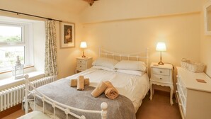 A bedroom with a bed, two bedside tables, a window with curtains, a radiator, and a wall-mounted light fixture. - White House (Penrith)