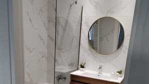 Une salle de bain moderne avec une douche à parois de verre, un meuble-lavabo en bois avec un miroir rond et un tapis de bain rose.