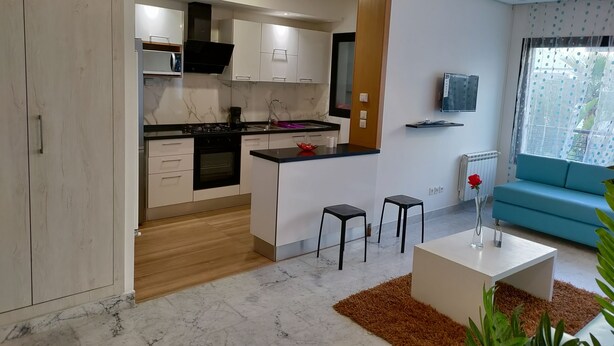 Une cuisine moderne avec des meubles blancs, une cuisinière noire et un plan de travail en marbre. On y trouve un petit îlot avec des tabourets, une table basse blanche et un canapé bleu.