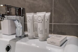 A bathroom sink with three tubes of shower gel and a box of toiletries.