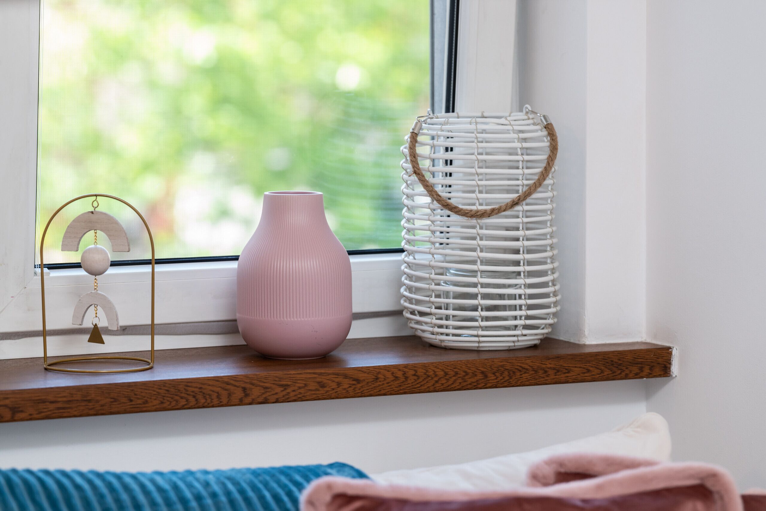 A window sill with a white wicker basket, a pink vase, and a gold-framed object.