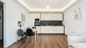 Een moderne keuken met witte kasten, een eethoek met tafel en stoelen, en een hanglamp.