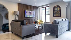 En moderne stue med to grå sofaer, et fladskærms-tv, en lampe og et bogskab.