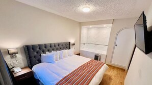 Et soveværelse med en stor seng, et natbord med lampe, et vindue med udsigt og en dør.
