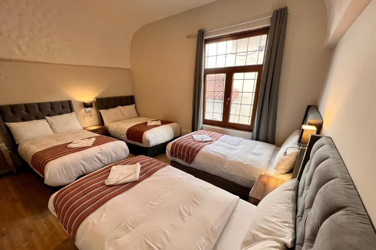 A hotel room with three beds arranged in a row, a large window with curtains, and a wooden floor.