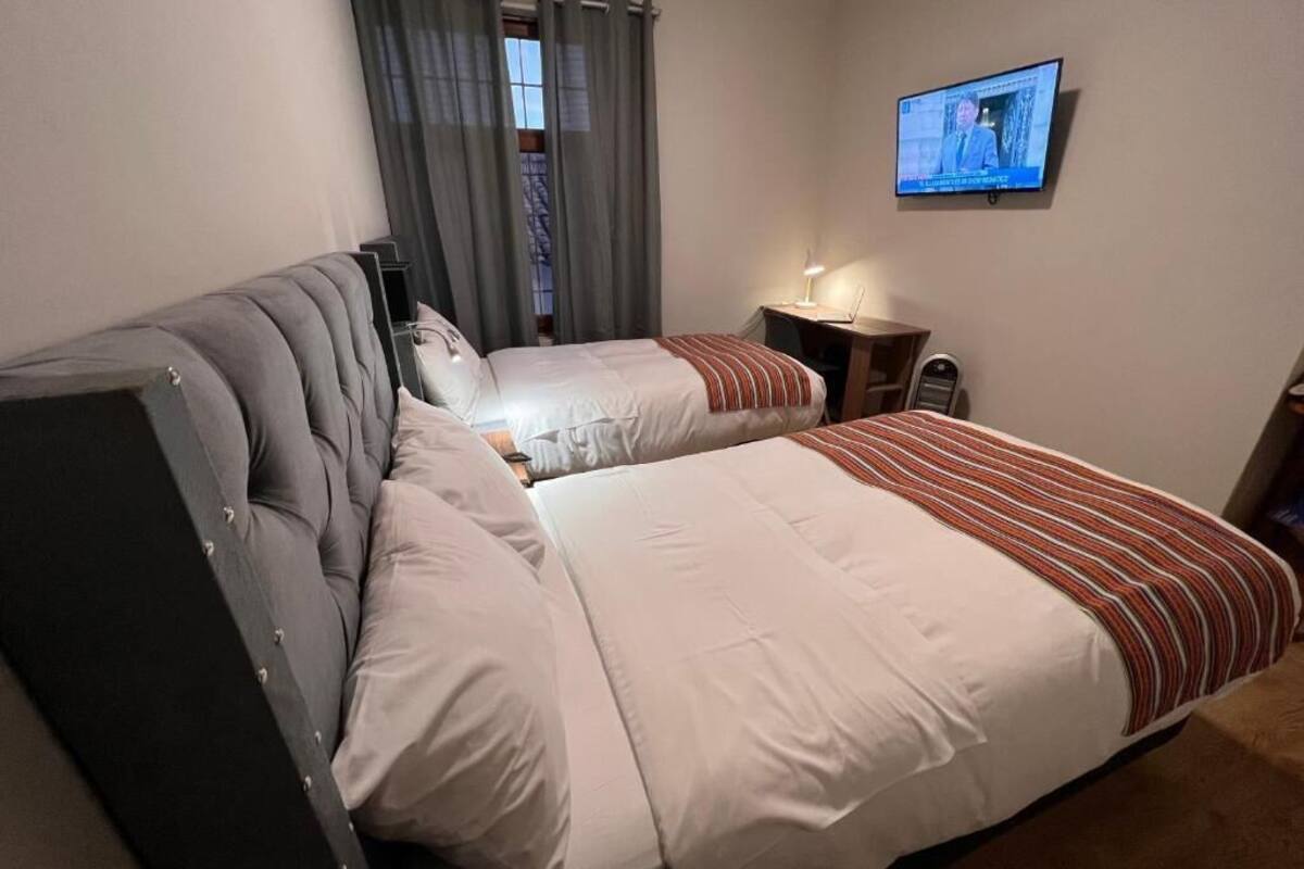 A hotel room with two beds, a television, a desk, and a window with curtains.
