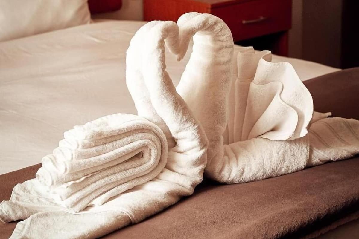 A neatly made bed with a swan-shaped towel arrangement on a brown bedspread.