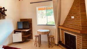 A cozy room with a television, a small table with stools, a fireplace, and a window with curtains. - Davilas Inn (Camanducaia)