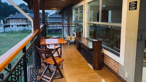 A wooden deck with a table and chairs, a trash can, and a view of a building with a sign. - Davilas Inn (Camanducaia)