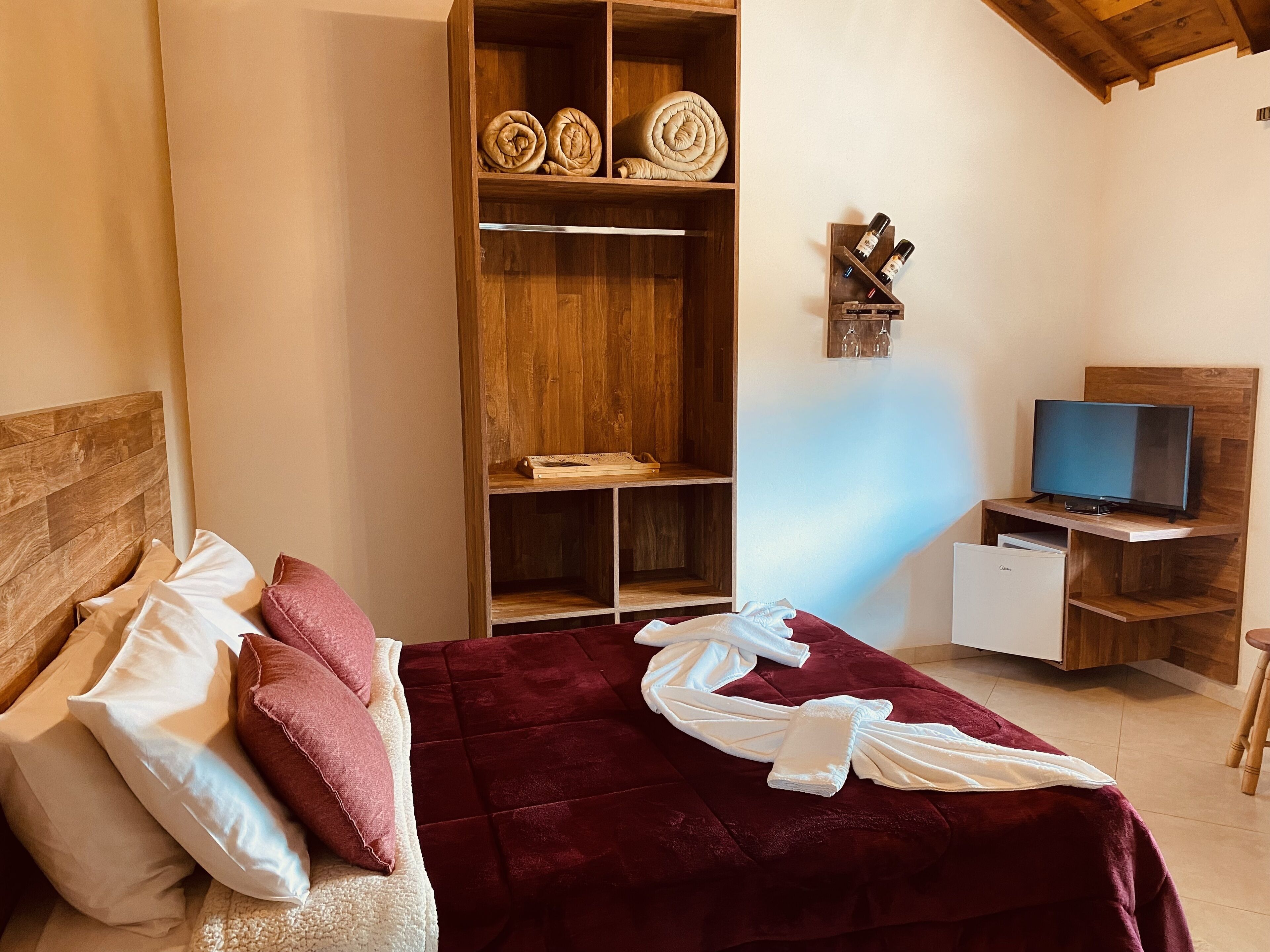 Un dormitorio con cama, armario, escritorio con televisor y un taburete pequeño.