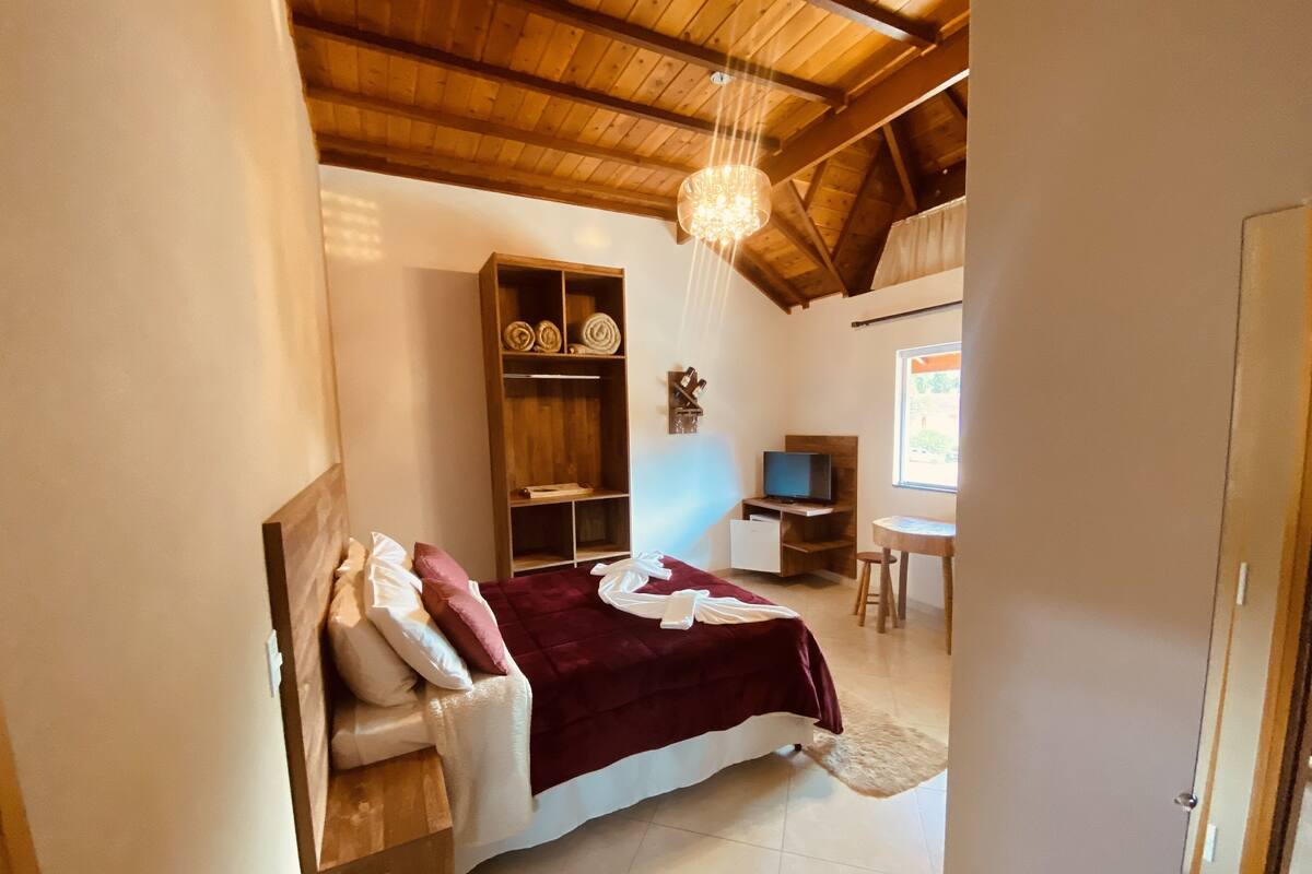 A bedroom with a bed, a wooden wardrobe, a television, and a small table.