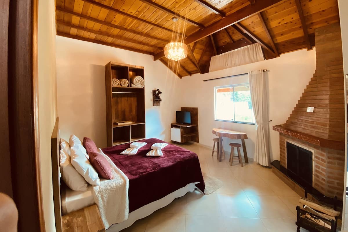 A cozy room with a bed, a wooden shelf, a television, a small table, a fireplace, and a window.