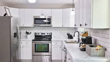 A modern kitchen with white cabinets, a stainless steel refrigerator, a microwave, a stove, and a sink.