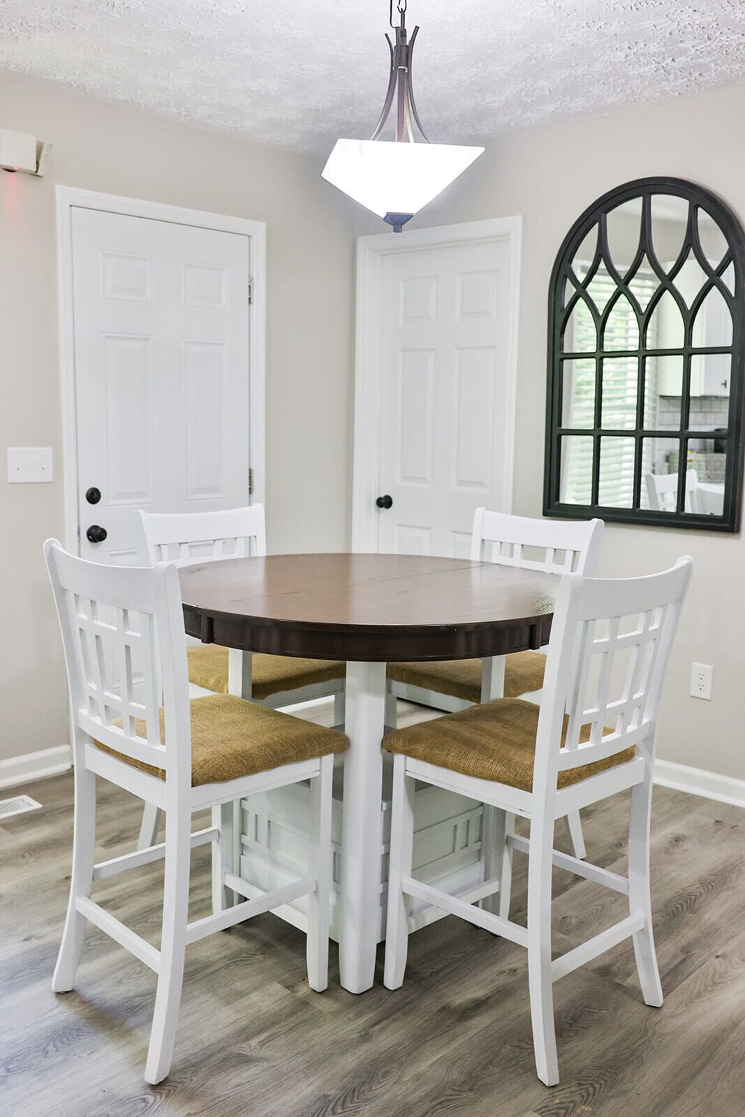A dining area with a round table and four white chairs with brown cushions.