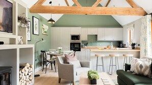 A cozy living room with a fireplace, a dining area, and a kitchen with white cabinets and a wooden ceiling. - 2 bedroom accommodation in Bramley, near Tadley (Bramley, near Tadley)