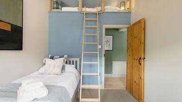 Una camera da letto con un letto a castello, una scala, un letto con lenzuola bianche, una parete blu, una porta in legno e un quadro appeso al muro.