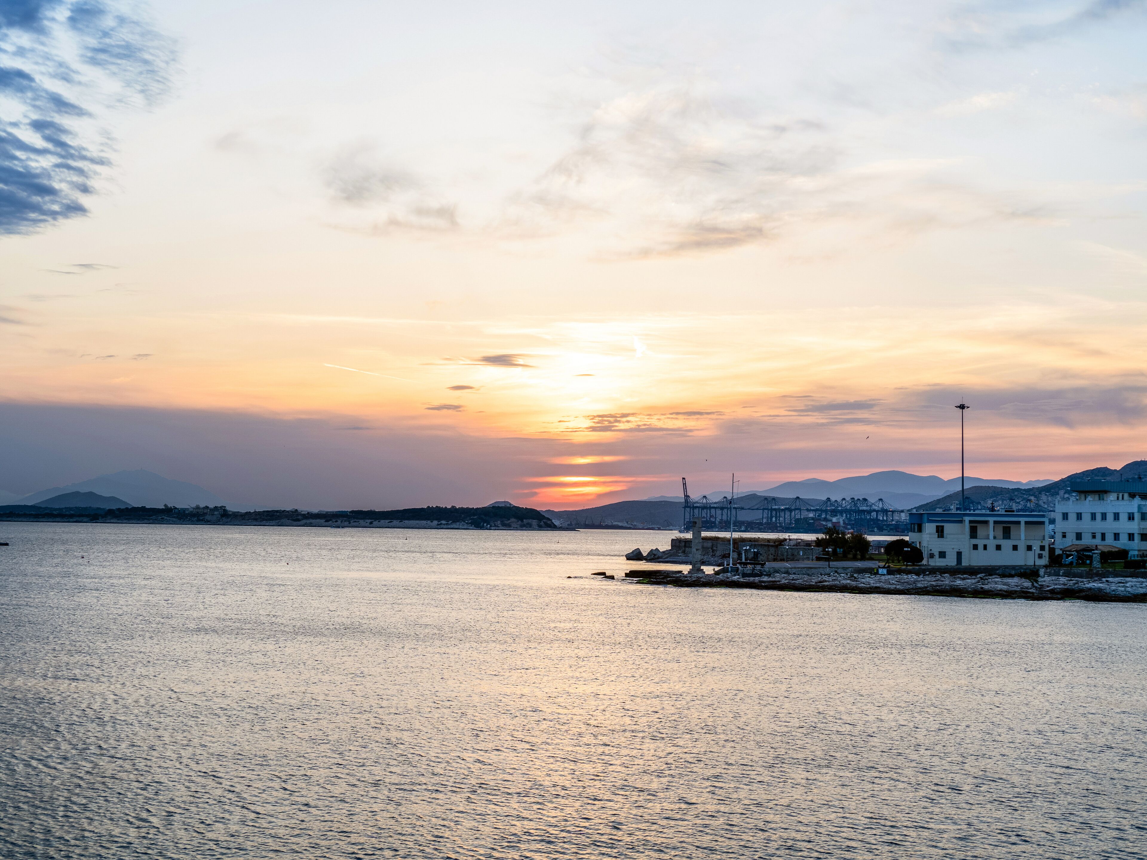 A waterfront view with a sunset, calm water, and distant mountains.