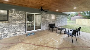 Varanda coberta com paredes de pedra, porta de correr de vidro que dá para um espaço interno e um ventilador de teto.