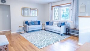 Ein modernes Wohnzimmer mit zwei Sofas, einem gemusterten Teppich und einem großen Fenster mit Vorhängen.