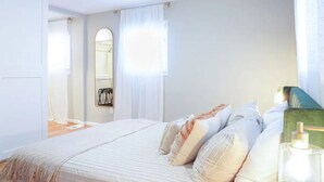 Ein Schlafzimmer mit einem Bett, einem Spiegel, einem Fenster mit Vorhängen und einem Nachttisch.