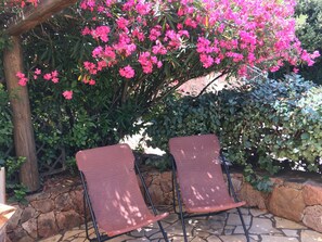 Zwei Stühle unter einer Pergola mit rosa Blüten und einer Steinmauer.