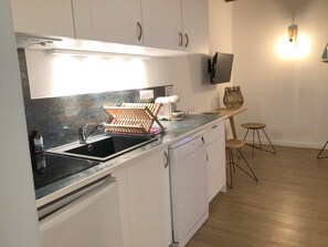 A modern kitchen with white cabinets, a black sink, and a dishwasher. There is a wooden rack on the countertop and a wall-mounted TV.