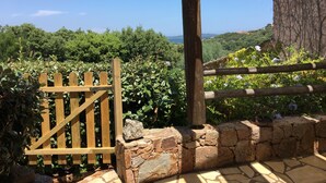 A wooden gate leading to a stone wall with a stone bench and a pair of sandals on it. - Apartment-Standard-Ensuite with Shower-Sea View-T2 (Porto-Vecchio)