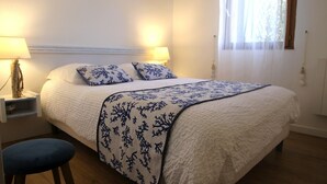 A neatly made bed with a white and blue floral bedspread, two matching pillows, and two bedside lamps on wooden nightstands. - Apartment-Standard-Ensuite with Shower-Sea View-T2 (Porto-Vecchio)