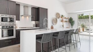 Een moderne keuken met donkere kastjes, roestvrijstalen apparatuur en een centraal eiland met barkrukken.