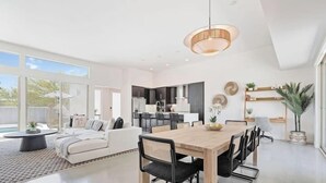 Een moderne keuken met donkere kastjes, een centraal eiland en een eethoek met een houten tafel en stoelen.