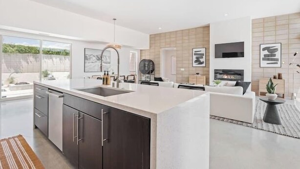 Een moderne keuken met donkere kastjes, een groot eiland en een zithoek met een bank en een salontafel.