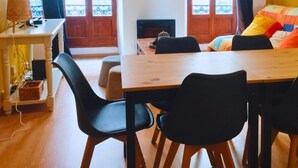 A cozy room with a wooden dining table, black chairs, a bed with colorful pillows, and a wall clock. - Appartement en Plein Centre (Carpentras)