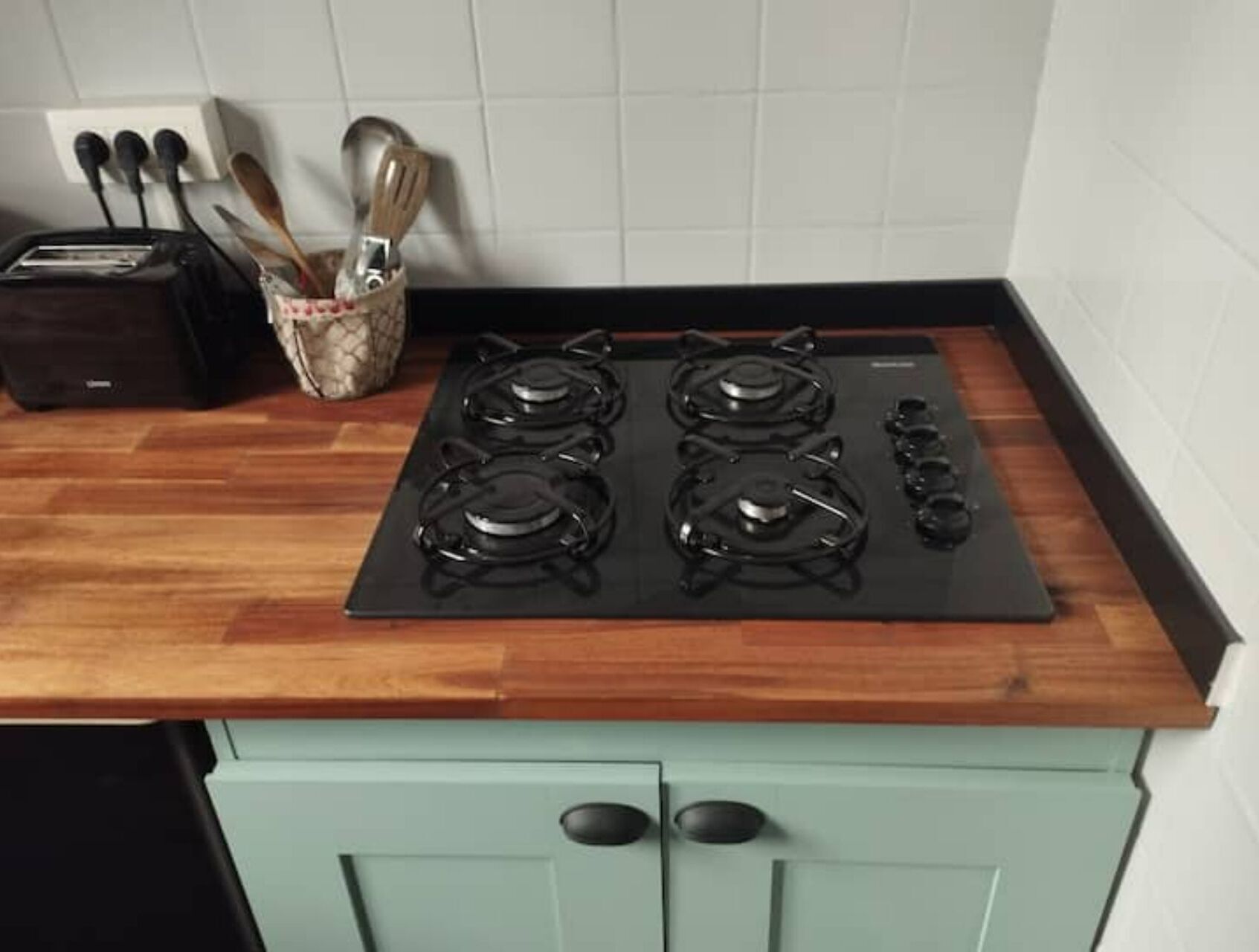 A kitchen with a black stove top, a toaster, and wooden utensils in a holder.