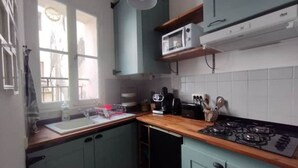 A kitchen with teal cabinets, a wooden countertop, a gas stove, a microwave, and a window with curtains. - Appartement en Plein Centre (Carpentras)