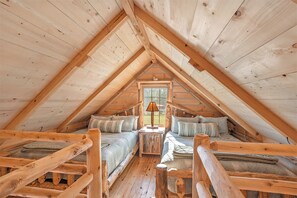 A cozy attic bedroom with wooden beams, two beds, a nightstand, and a window.