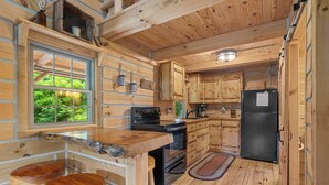 Interior de una cabaña de madera con cocina, barra y ventana con vistas a follaje.