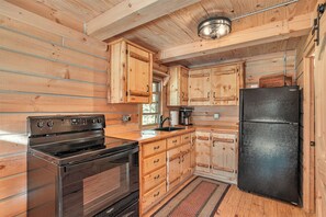 A wooden cabin interior with a kitchen featuring a stove, refrigerator, and wooden cabinets.
