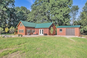 A two-story log cabin with a green roof, a front porch, and a garage.