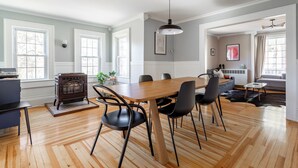Amplia sala de estar con una mesa de comedor de madera, sillas negras, una chimenea y ventanas grandes.
