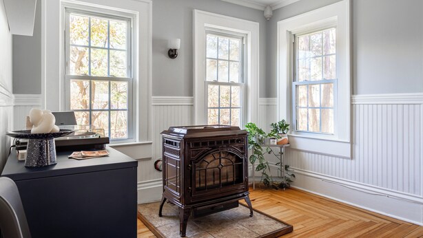Una habitación con estufa antigua, ventanas amplias y suelo de madera.